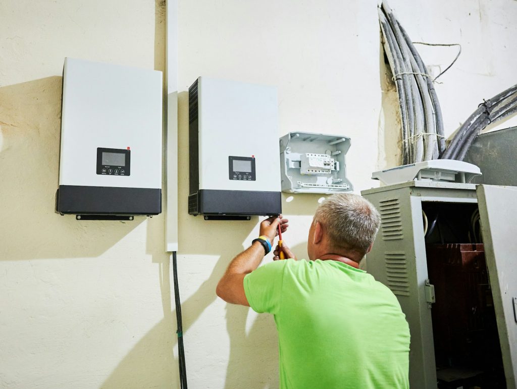 Man electrician wiring inverter and electric box indoors while installing solar panel system.